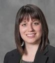 white female with should length dark brown hair and bangs; black jacket; green eyes; smiling 